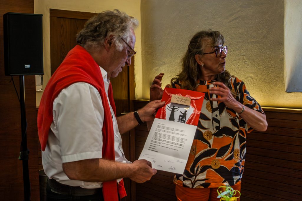 Karin E. Götz übergibt Opernliebhaber Dr Wolfgang Lorenz als Abschiedsgeschenk einen Gutschein für einen Opernbesuch seine Wahl
